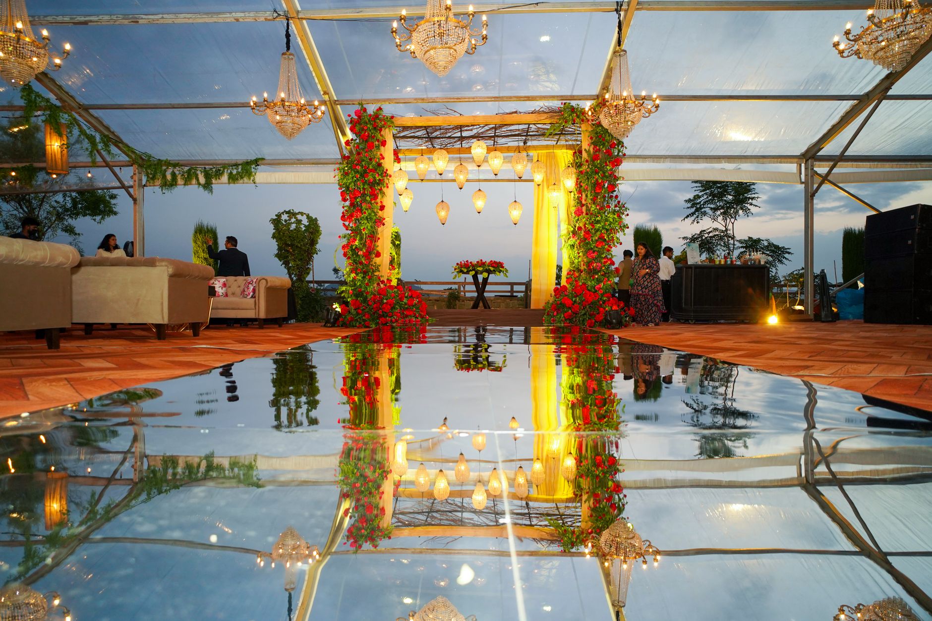 Chic indoor event setup with chandeliers, floral decor, and mirrored reflections during dusk. — Apuestas Liga De Campeones