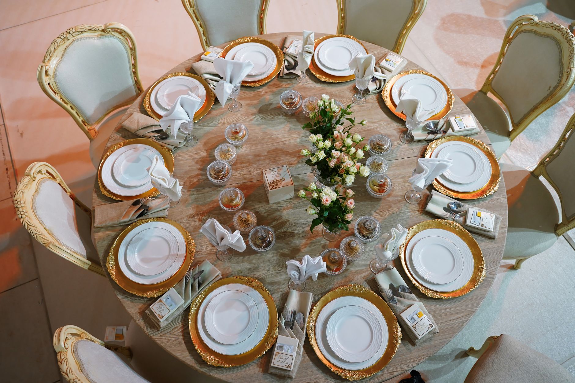 Luxurious round table with golden plates and roses, meticulously set for a wedding celebration. — Europese Competitie Wedden