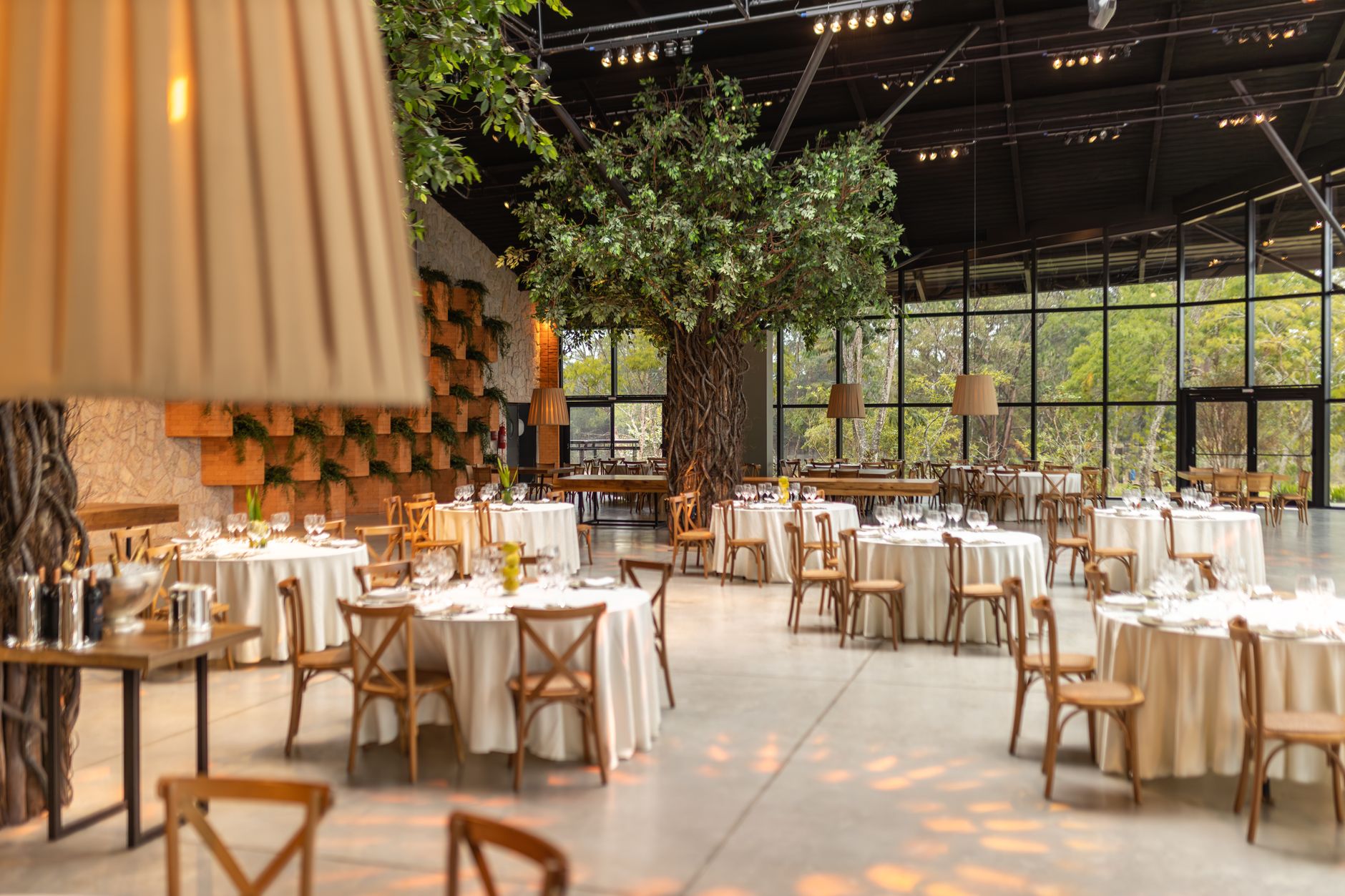 Spacious event hall featuring round tables, chairs, and indoor trees. Ideal for weddings or conferences. — Universidad De Chi